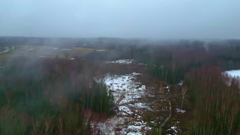 Vista-Aérea-Brumosa-Sobre-Un-Escaso-Paisaje-Invernal-Al-Amanecer,-Parches-De-Nieve