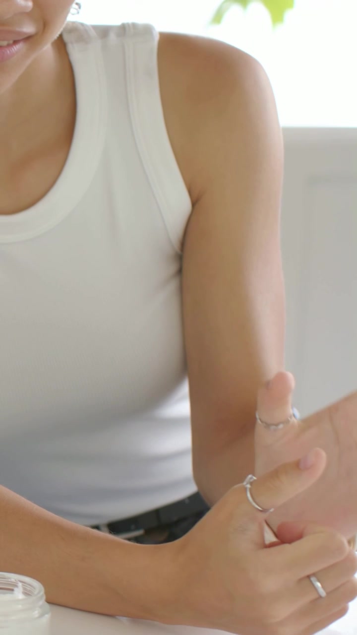 Video verticale: Donna con canotta bianca, con le braccia appoggiate, che fa girare un anello e tocca l'orologio su un bancone luminoso.