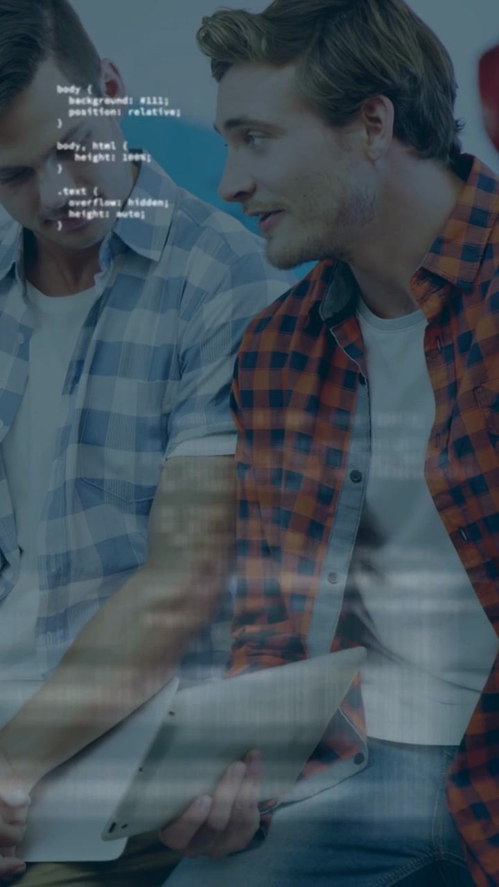 Vertical video: Man in red shirt tapping tablet, peer leaning in, code overlay driving tech demo