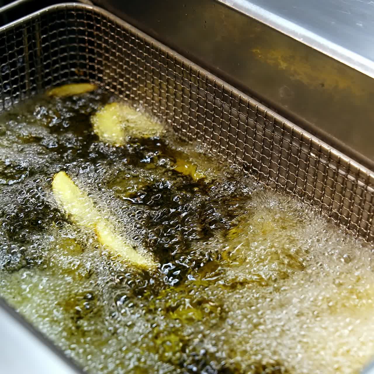 Cooking in deep fryer. Golden potato frying in a hot boiling oil in the restaurant. Crispy vegetables in deep fryer. Unhealthy food