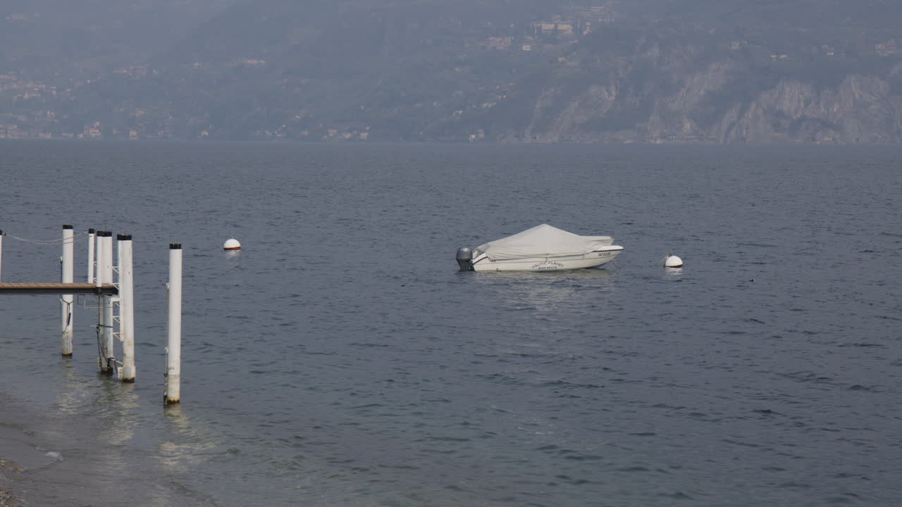 Boat Covered With Tarp Floating Near Shore Of Lake Como In Italy. wide shot