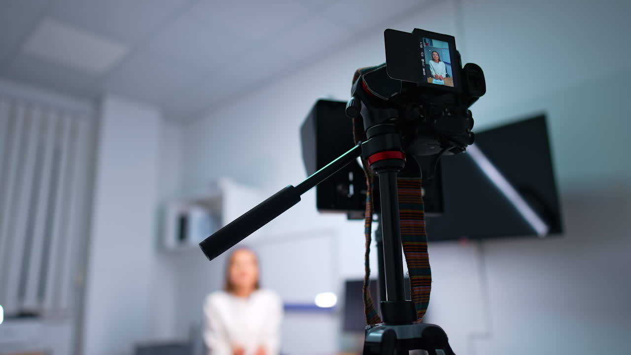 Modern camera on tripod recording video blog. Low angle view. Woman influencer creates content for a vlog. Blurred backdrop.