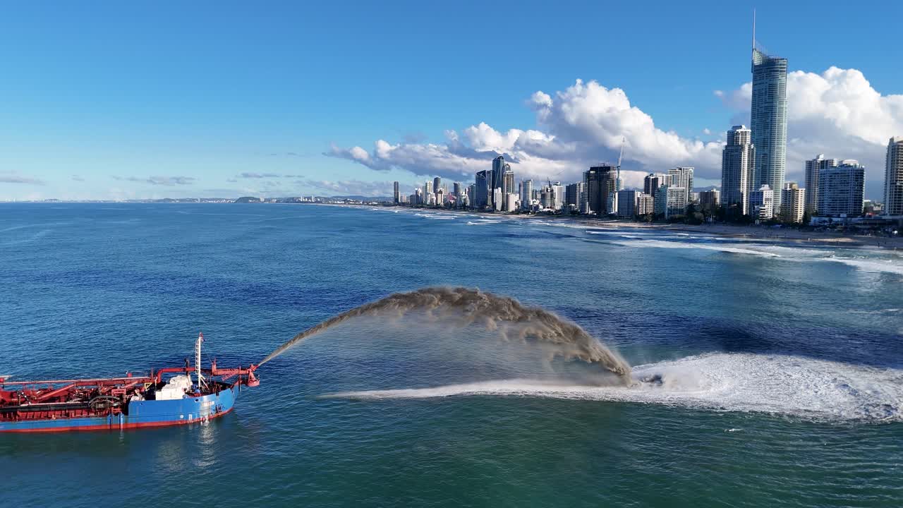 A dredging vessel pumps sand into the ocean near the Gold Coast skyline under clear blue skies
