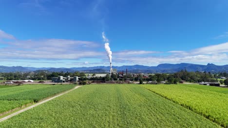 drone footage captures expansive green fields with a distant factory emitting smoke under clear blue skies
