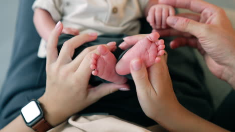 mother plays with adorable tiny feet of her child. male hand touches the kid's hand. close up.