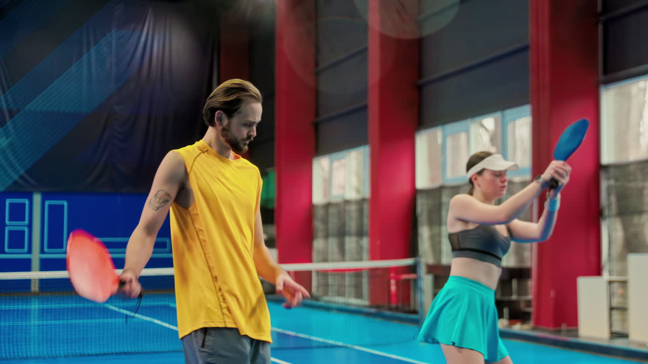 A man teaching a woman how to play pickleball in an inside court
