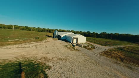 Flying-over-large-chicken-barn-with-FPV-drone-at-sunset-on-midwestern-egg-farm,-henhouse-and-feeders-aerial-4k