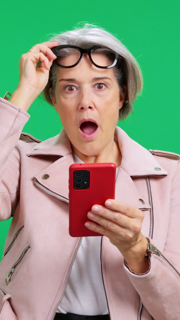 Donna matura che reagisce con shock e sorpresa al contenuto dello smartphone.