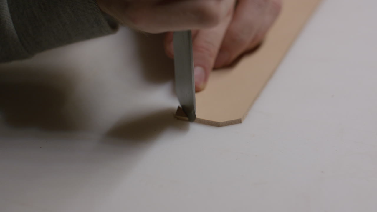 A leatherworker carefully trims the edge of a leather strip with a sharp knife, ensuring clean and accurate cuts in the crafting process.