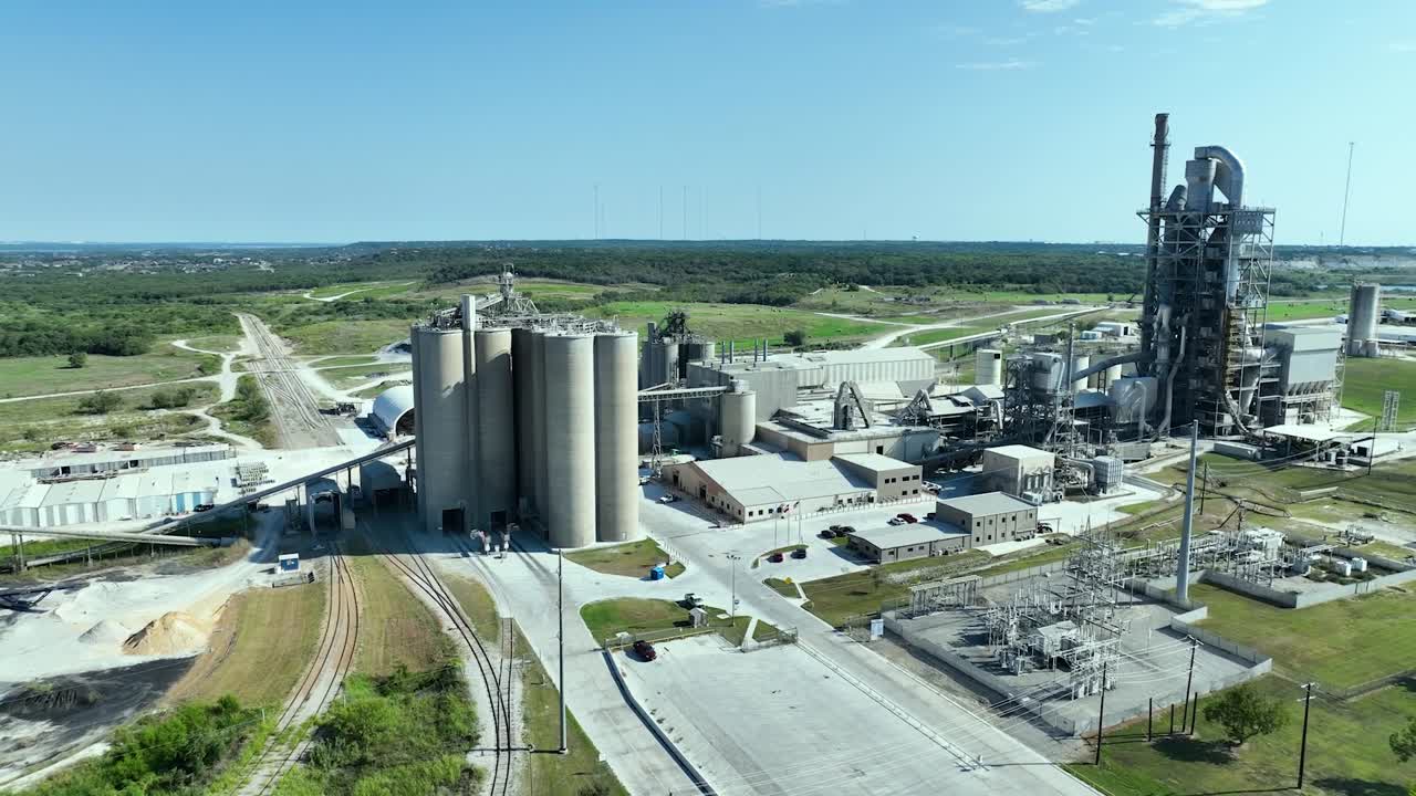 Luftaufnahme eines großen industriellen Zementwerks mit Silos und Bahngleisen unter klarem blauem Himmel