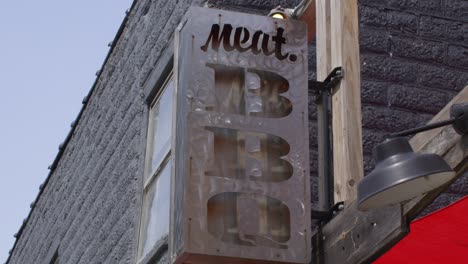 Meat-BBQ-restaurant-sign-in-Lansing,-Michigan-Old-Town-district-with-stable-establishing-shot-looking-up