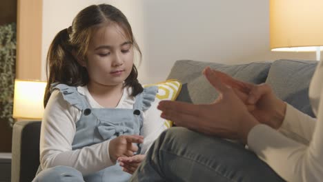 profesor o padre enseñando lenguaje de señas a una niña sentada en un sofá en casa 1
