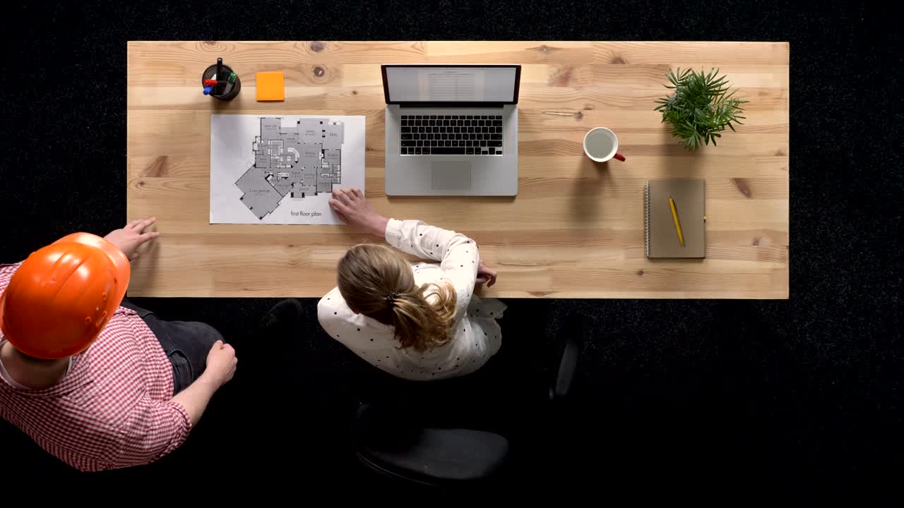Young businesswoman is working on laptop in daytime, builder comes and they discuss plan of building, work concept, office concept, communication concept, top shot