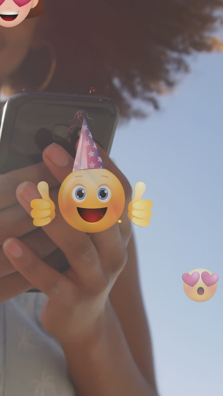 animación de emoticones sobre la sección media de una mujer biracial que usa un teléfono inteligente al aire libre