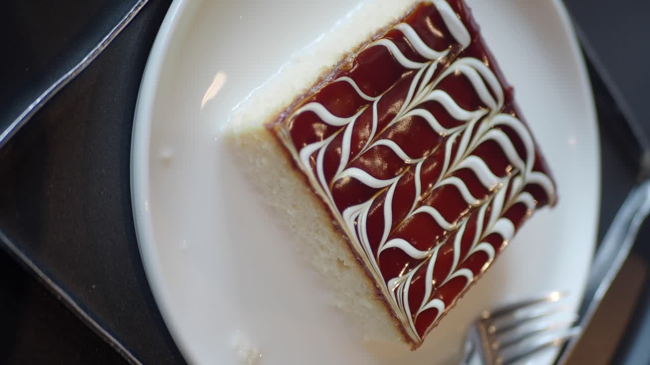 A slice of dessert with red glaze and white swirled icing on a white plate