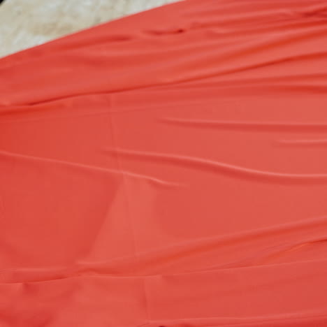 professional tailor layng bright red fabric on a table. work place table of sewer and a big piece of red cloth in workshop.