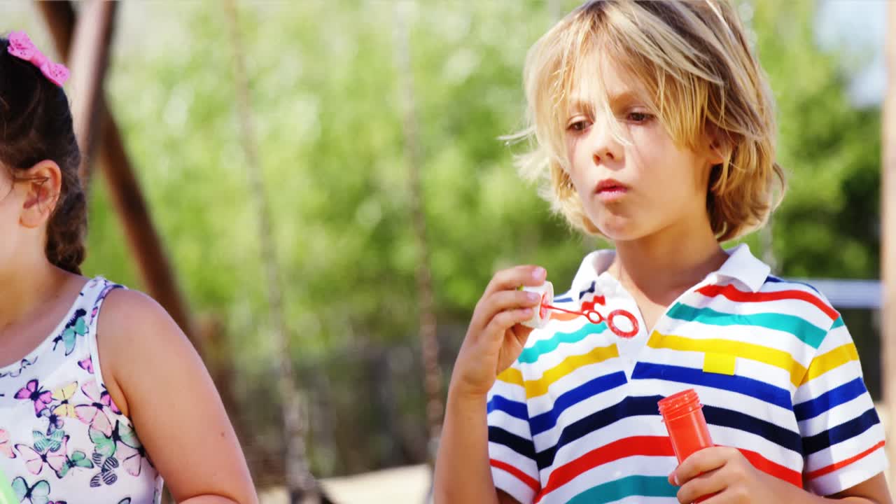Bambini che giocano con la bacchetta per bolle di sapone al parco giochi