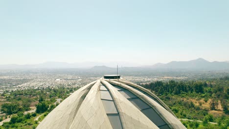 Aerial-boom-up-view-of-the-top-of-the-Bahai-Temple-of-South-America-with-the-city-of-Santiago-clean,-without-smog-on-a-sunny-day