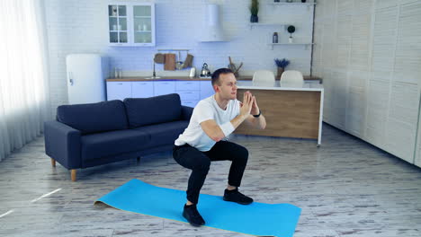 young man exercising on fitness mat at home. active male in white t-shirt and black pants doing his workout on quarantine on kitchen background. sport, fitness and healthy lifestyle at home.