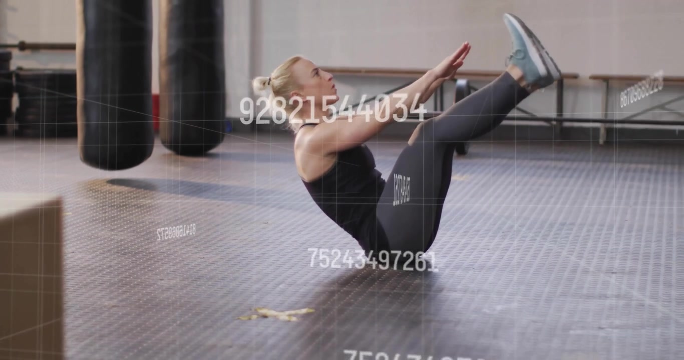 Mid-adult woman contracting abs, curling into V-sit on rubber mat in gym demonstrating core control