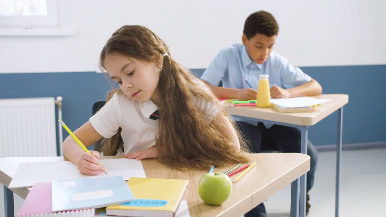 niña pequeña escribiendo en un cuaderno, luego pensando en algo y suspirando durante la clase de inglés en la escuela