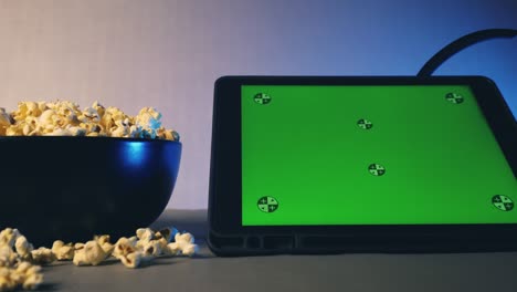 tablet computer with green touch screen and popcorn in a big bowl on sofa.