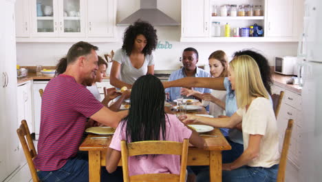 dos familias con niños adolescentes comiendo comida en la cocina