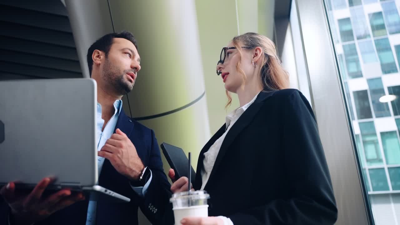 Well dressed young professionals talk in hallway discussing report on computer on way into office