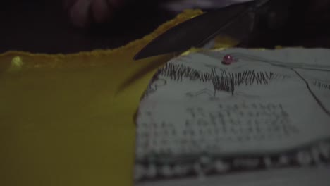 old lady tailor use scissors to cut yellow fabric, with needle and newspaper