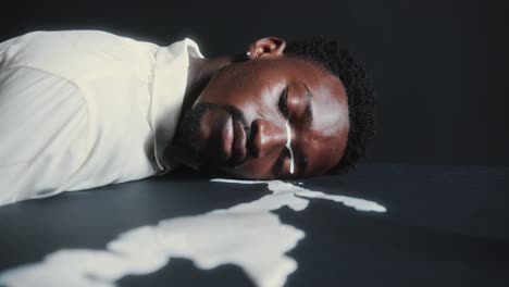 black man lying down on dark floor and crying with white paint