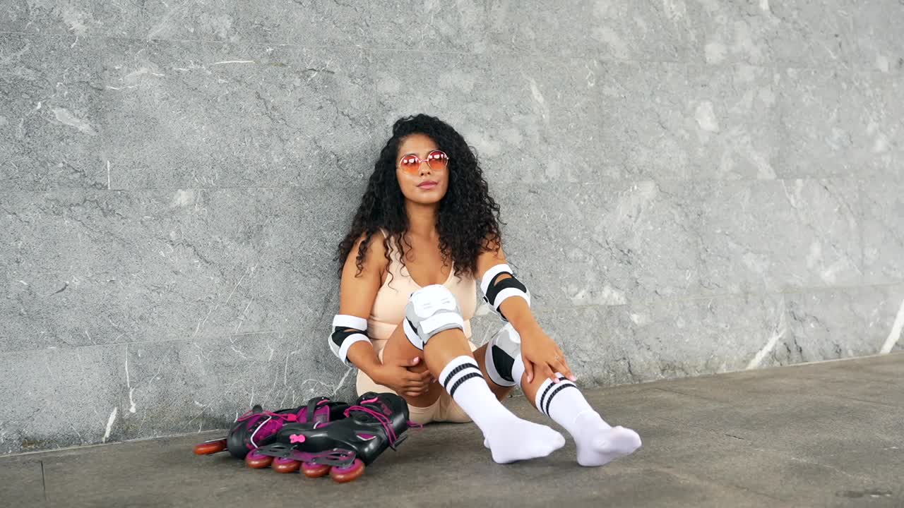 Mulher com patins e equipamento de proteção sentada em uma parede