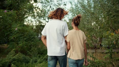 Shooting-from-behind:-A-girl-with-her-curly-boyfriend-in-a-white-T-shirt-are-walking-in-the-country-house