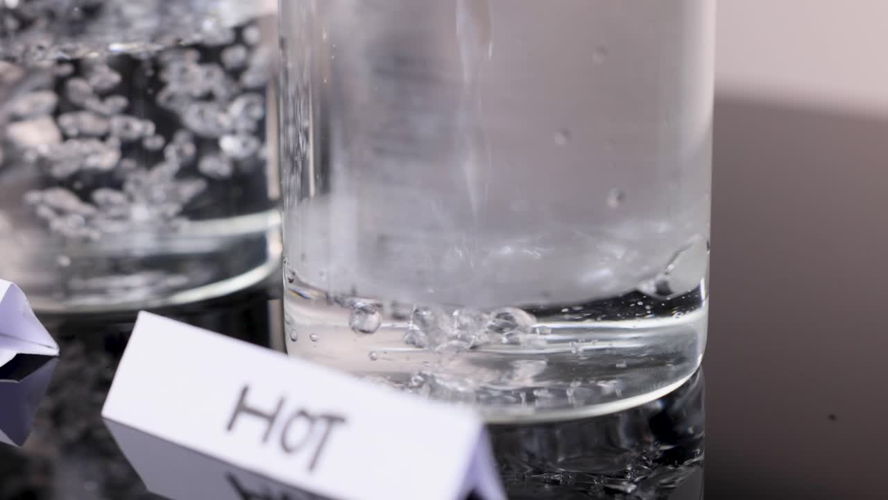 Hot water poured into clear glass beaker, creating swirling motion, under bright studio lighting