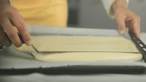 chef spreading a beige biscuit dough on a baking sheet