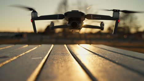 black mavic 2 on table outdoors starting up and taking off, with a blurred sunset and country background