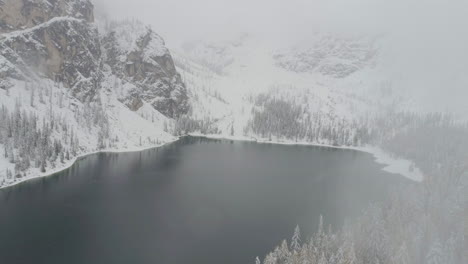 Aerial-view-establishing-through-clouds-to-snow-covered-Italian-Lago-Di-Braies-mountain-forest-lake-South-Tyrol