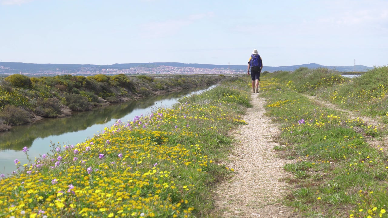 Un escursionista cammina attraverso il paesaggio della Salina di Sant'Antioco sull'isola di Sant'Antioco in Sardegna, Italia, circondato da saline e terreno naturale.