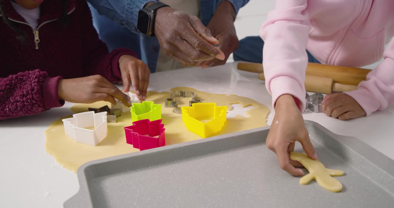 Adult placing tray on kitchen counter is starting hands pressing cutters into rolled dough to bake