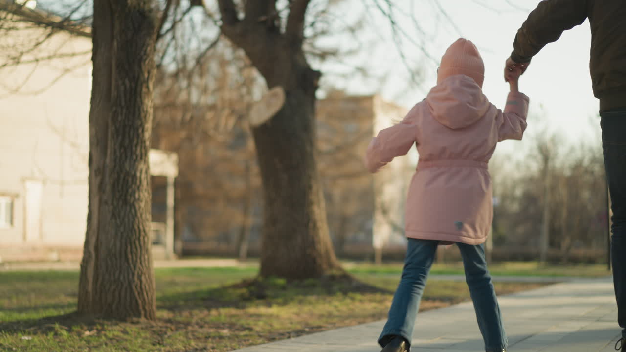 분홍색 모자와 재을 입은 어린 소녀가 갈색 재과 파란 청바지를 입은 남자와 함께 걸어가는 장난스러운 순간.