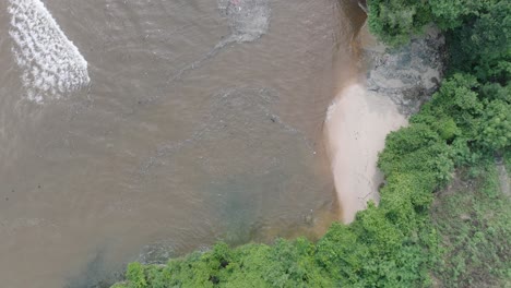 Slow-motion-high-altitude-top-down-drone-shot-of-polluted-ocean-filled-with-floating-trash-and-debris-and-muddy-sewage-runoff-with-green-tropical-forest-and-beach-in-Bali-Indonesia