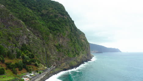 Costa-Con-Cascada-Olas-Acantilado-Montañas-En-Las-Nubes-Horizonte-Panorámico-Del-Océano-Cielo-Panorámico-Levantamiento-Drone-Shot-Madeira