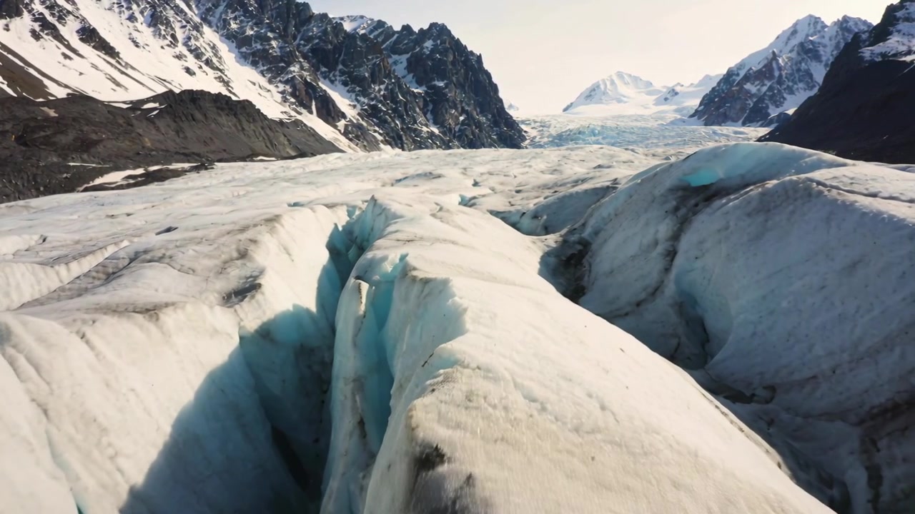Gleitende Drohne bewegt sich vorwärts entlang eines zentralen Eisgrats an einem Alpengletscher, um eine tiefe Gletscherspalte zu enthüllen.
