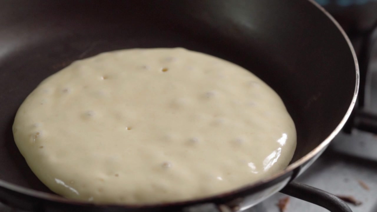 Close-up de massa de panqueca cozinhando em frigideira antes de virar. Bolhas de ar se formando na superfície enquanto o café da manhã cozinha no fogão em ambiente de cozinha interna.
