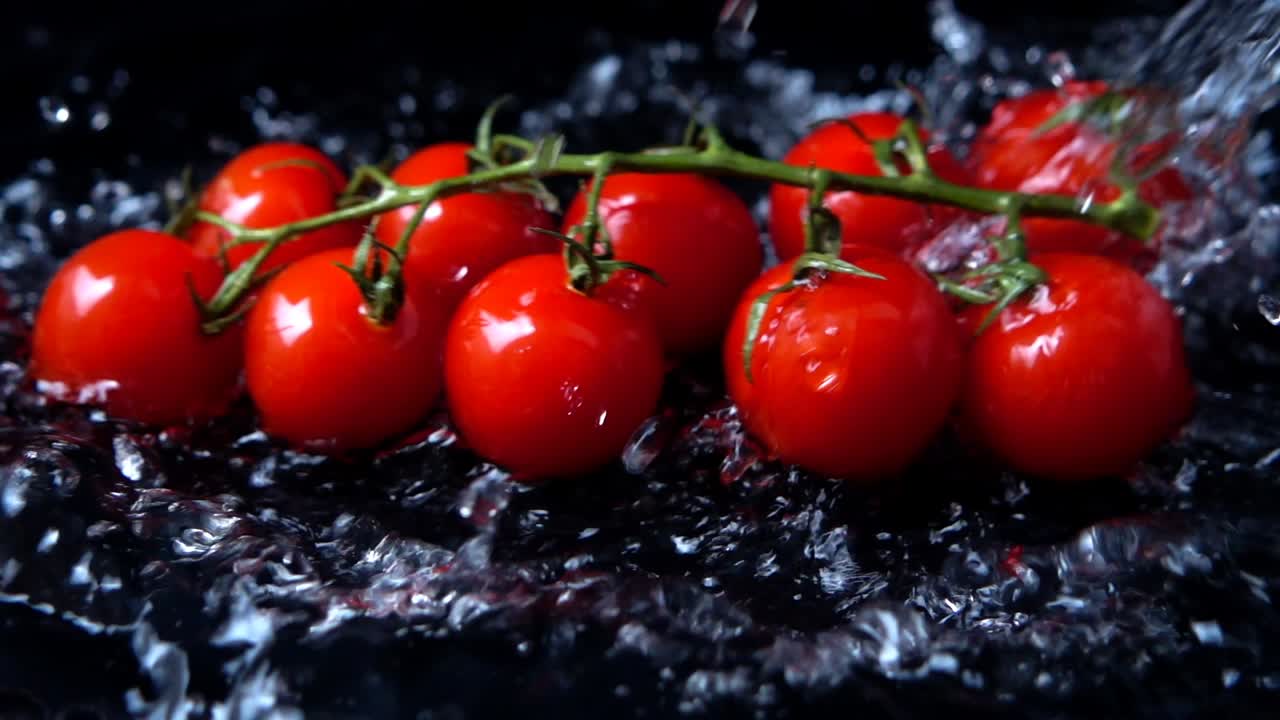 I pomodorini ciliegino che cadono nell'acqua su uno sfondo nero. Slow motion