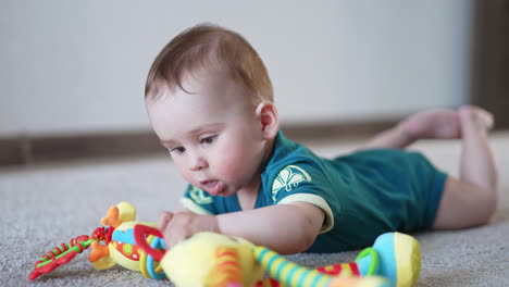 cute sweet child lies on the floor indoors. adorable baby pulling bright toy to his mouth. blurred backdrop.