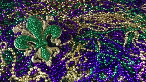 Sparkling-fleur-de-lis-in-green-on-pile-of-colorful-Mardi-Gras-beads