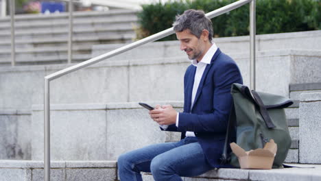 hombre de negocios sentado afuera en la pausa para el almuerzo usando un teléfono móvil