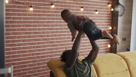 joyful father raising his toddler son up in air while sitting on sofa