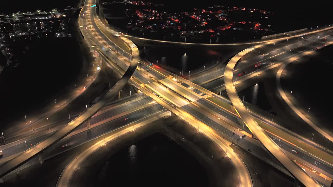 An aerial view of a large stack interchange on Florida's Turnpike on a clear night. The camera dolly in, boom up and tilt down over the intersection and retention ponds in the landscape