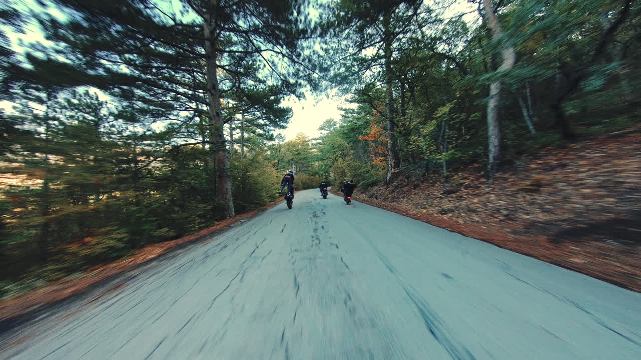 Action shot as the camera follows a crew of stunt bikers riding down a forest road